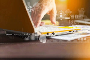 Data Graphics Laptop A hand typing on a laptop keyboard with digital data graphics overlay, including charts, binary code, and icons, representing technology and data analysis.